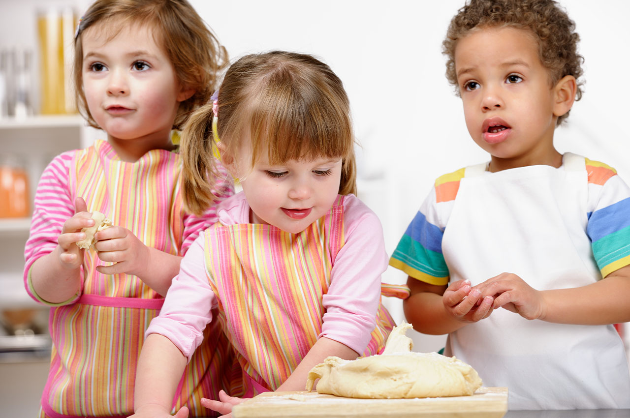 three small children in apron rolling dough