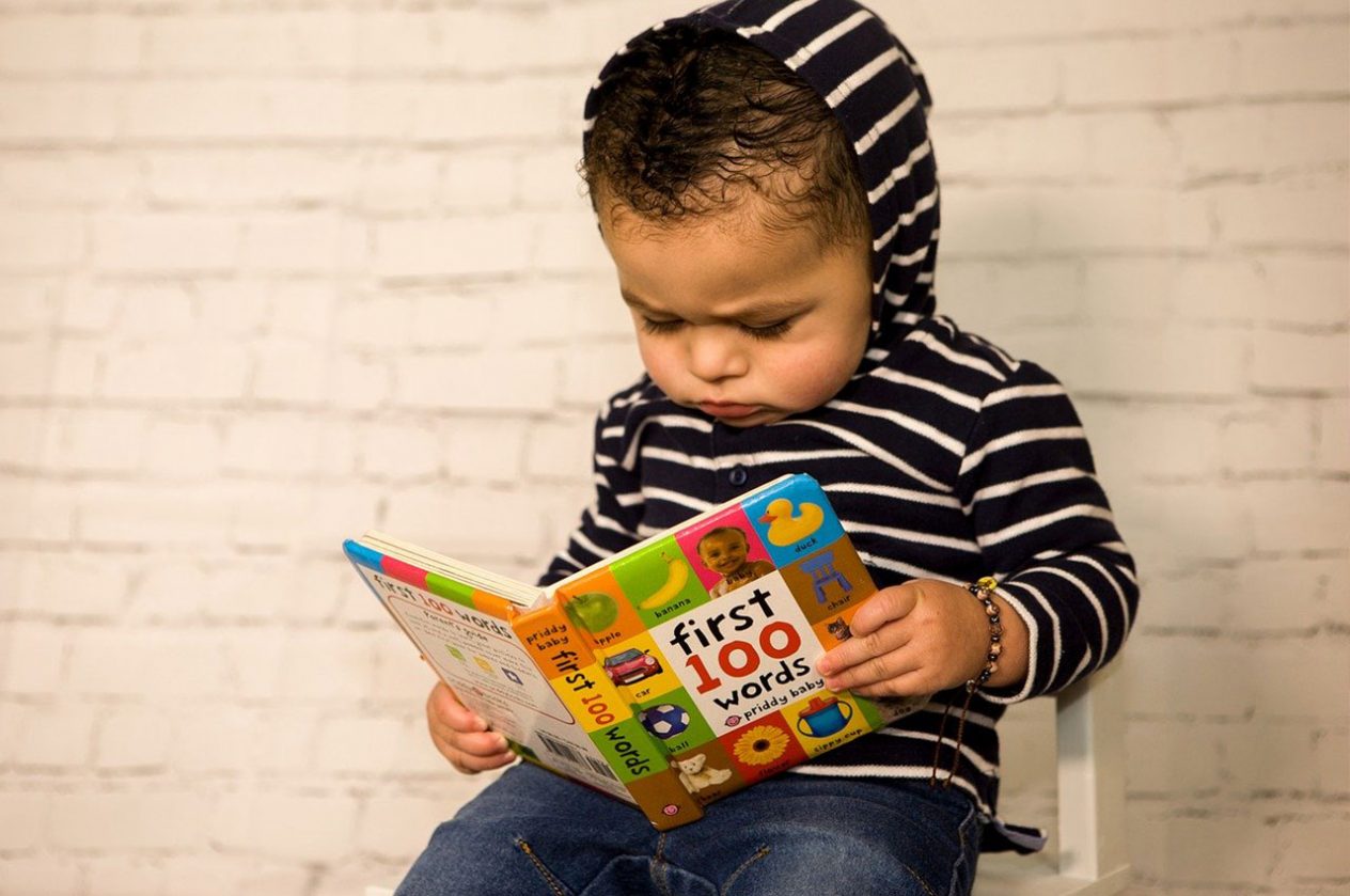 child sitting on chair reading my first 100 words children's early literacy book
