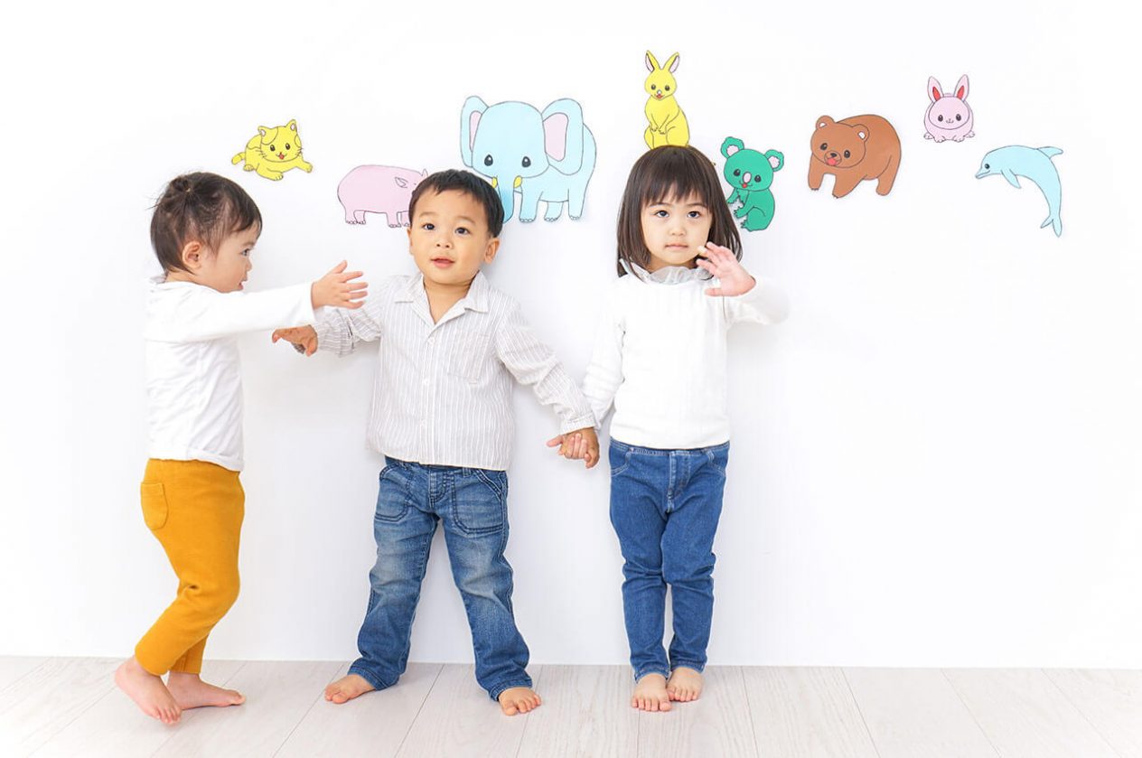 3 asian toddlers standing against wall