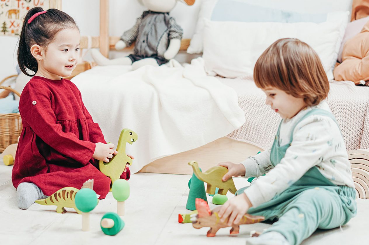 two children playing with wooden dinosaur toys